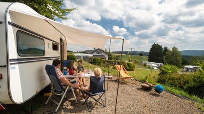 Eine Familie sitzt im Campingpark im Bergischen Land vor ihrem Wohnwagen