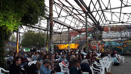 Zuschauer sitzen unter dem Gebäudeskelett einer alten Industriehalle auf dem Hawerkamp in Münster