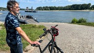 Ein Mann steht mit einem Fahrrad an einem Bootsanleger am Rhein