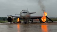 Die Brandsimulationsanlage der Flughafenfeuerwehr Düsseldorf: An einem ausrangierten Flugzeug schlagen an einem Reifen und aus einem Triebwerk lodernde Flammen empor.