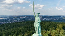 Die Statue des Hermannsdenkmals mit erhobenem Schwert, im Hintergrund die Stadt Detmold