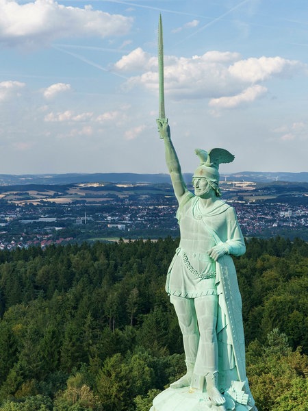 Die Statue des Hermannsdenkmals mit erhobenem Schwert, im Hintergrund die Stadt Detmold