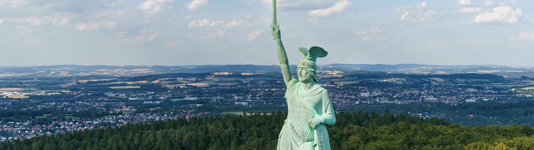 Die Statue des Hermannsdenkmals mit erhobenem Schwert, im Hintergrund die Stadt Detmold