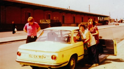 Ein Archiv-Foto, das drei Menschen an einem alten Auto zeigt