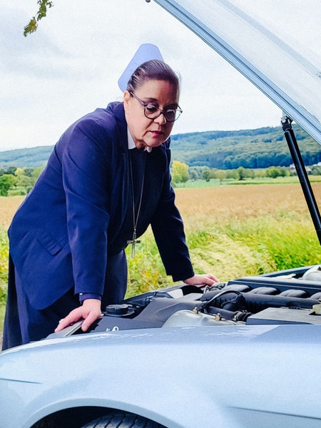 Eine Frau steht an der geöffneten Motorhaube eines Autos