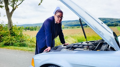 Eine Frau steht an der geöffneten Motorhaube eines Autos