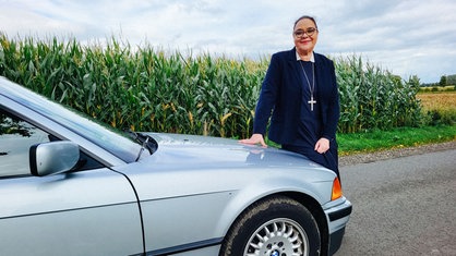 Die Glaubensschwester Andrea Brewitt steht an der Front ihres BMW-Oldtimers und lächelt in die Kamera.