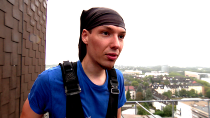 Industriekletterer Phillipp Brühl steht mit einem Tuch auf dem Kopf auf einem Hochhaus in Essen, im Hintergrund sind die Häuser der Stadt zu sehen