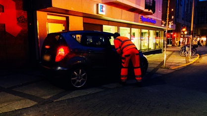 Ein Mann in Arbeitskleidung spricht mit einer Autofahrerin.