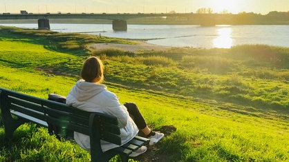 Eine Frau sitzt auf einer Bank und blickt auf die Sandbuchten und den Rhein hinunter.