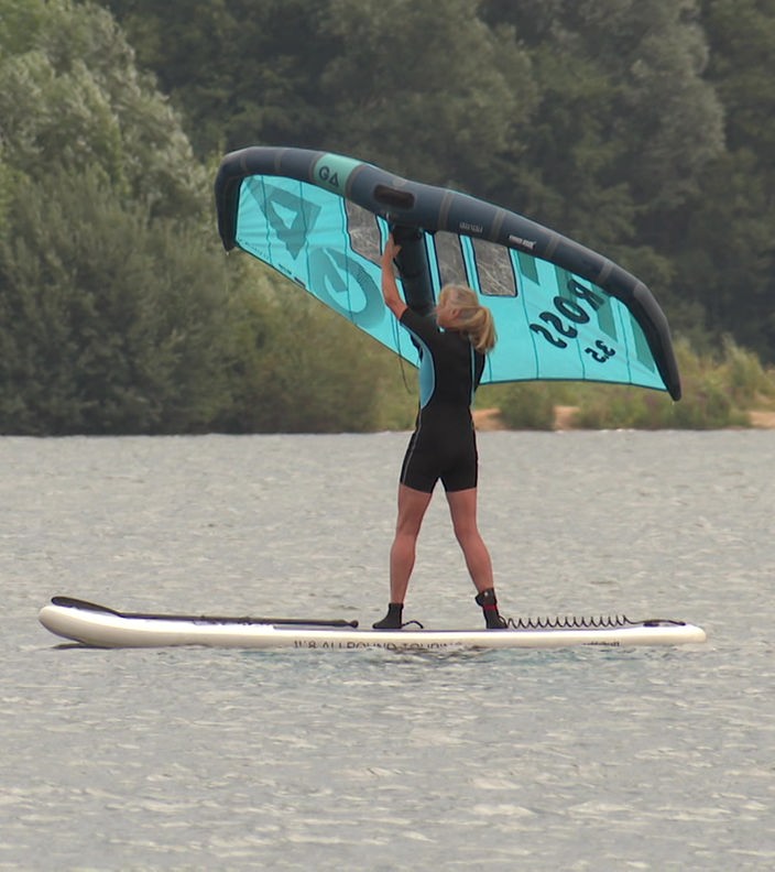Eine Frau steht auf einem Stand-Up-Board und hält dabei ein Segel in den Wind.