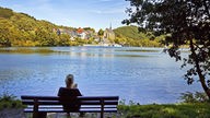 Ein Frau sitzt auf einer Bank am Beyenburger Stausee und genießt die Aussicht