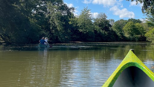 Ein Kanu fährt auf einem Fluss unter blauem Himmel 