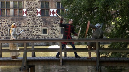 Zwei Männer in Mittelalterkostümen trainieren Schwertkampf auf einem Holzsteg vor der Burg Vischering.