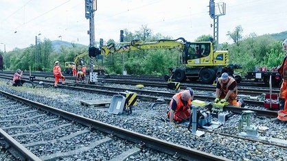 Bauarbeiter knien auf Bahnschinen. Ein Kran im Hintergrund.