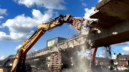 Ein Bagger reißt eine Brücke ab, Teile der Brücke fallen zu Boden