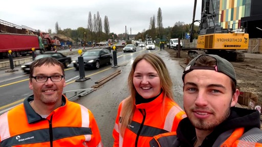 Zwei Männer und eine Frau stehen auf der Brückenbaustelle auf der B51 in Münster, im Hintergrund fahren Autos