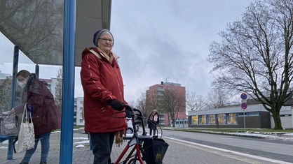 Seniorin wartet mit ihrem Rollator an einer Bushaltestelle