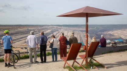 Mehrere Menschen stehen mit dem Rücken zur Kamera am Aussichtspunkt Terra Nova 1 und blicken auf den Hambacher Tagebau.