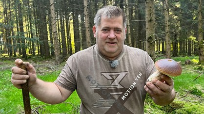 Der Pilzsachverständige Rainer Wald steht im Wald und hält einen Steinpilz in der Hand
