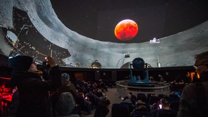In einem Planetarium bestaunen viele Menschen den Livestream des Blutmondes.