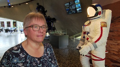 Martina Münch steht im Umlauf des Planetariums in Bochum, neben ihr der Anzug eines Astronauten