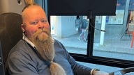 Busfahrer Alex Menschel sitzt am Steuer und lächelt 