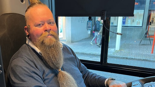 Busfahrer Alex Menschel sitzt am Steuer und lächelt 