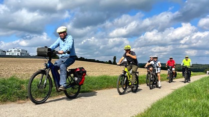 Mehrere Radfahrer fahren hintereinander über einen Feldweg