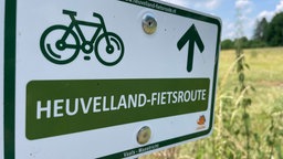 Auf einem Schild an einer Wiese steht "Heuvelland-Fietsrout".