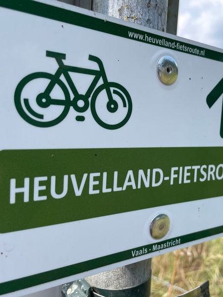 Auf einem Schild an einer Wiese steht "Heuvelland-Fietsrout".
