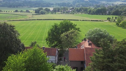 Aus der Vogelperspektive ist ein alter Bauernhof zu sehen. Im Hintergrund eine grüne Wiese und am Horizont ein Wald.