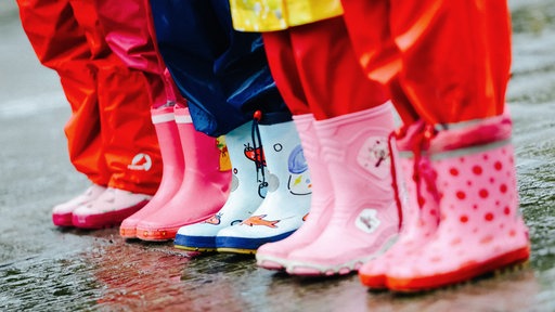 Die Beine von fünf Kindern in Regenkleidung nebeneinander.