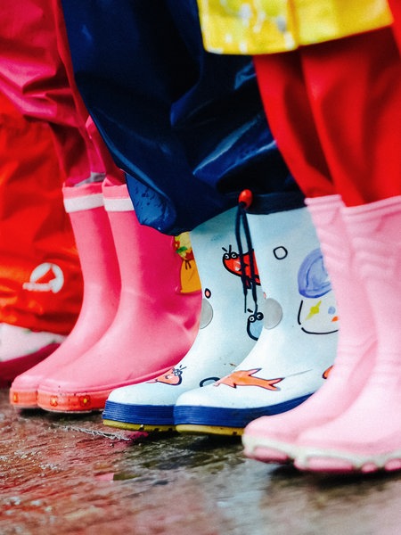 Die Beine von fünf Kindern in Regenkleidung nebeneinander.