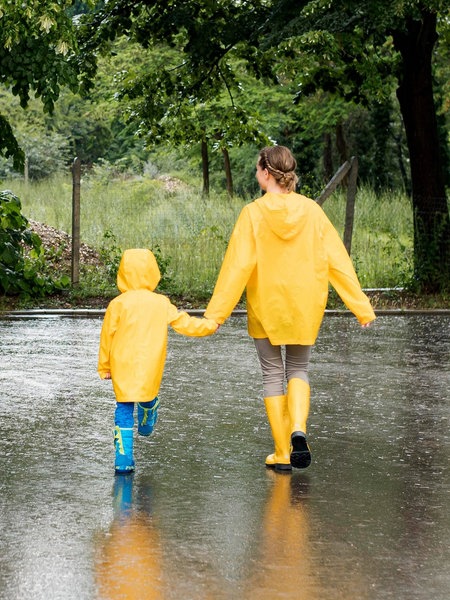 Ein kleines Kind und eine junge Frau laufen Hand in Hand mit Regenmänteln durch den Regen