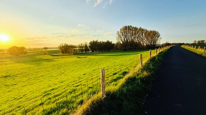 Eine Landschaft bei Sonnenuntergang. Rechts ein Wanderweg