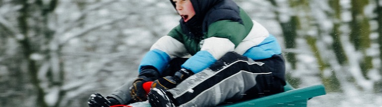 Eine Junge rodelt auf seinem Schlitten einen Berg hinunter.