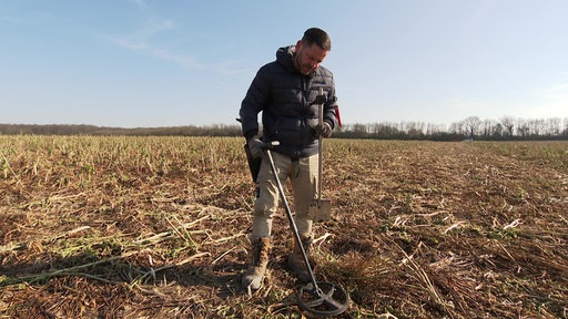 Carsten Konze sucht auf einem Feld bei Pulheim mit einem Metalldetektor den Boden ab.