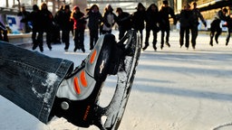 Ein Fuß mit einem Schlittschuh, im Hintergrund weitere Menschen mit Schlittschuhen und die Zeche Zollverein