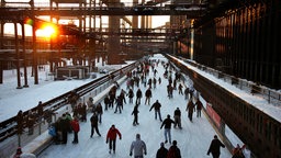 Auf der Eisbahn vor der Zeche Zollverein in Essen fährt eine Gruppe von Besuchern Schlittschuh