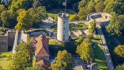 Luftaufnahme der Sparrenburg. Zentral steht  ein großer Turm aus Stein, darum mehrere Häuser.