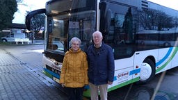 Ein Seniorenpaar steht vor einem Schulbus