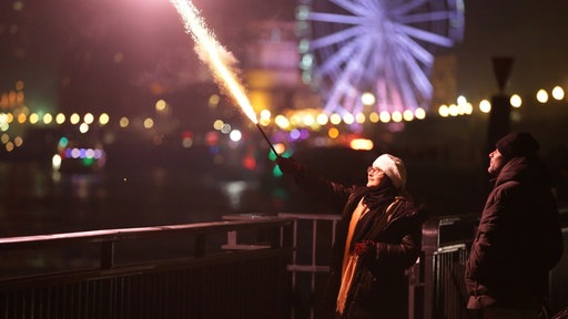 Eine junge Frau mit Feuerwerk in der Hand am Rhein in Düsseldorf