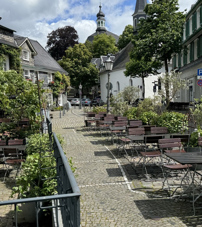 Eine Altstadt-Szene in Solingen-Gräfrath mit Kopfsteinpflaster, Fachwerkhäusern und einer Außengastronomie. 