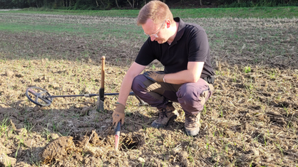 Constantin Fried hockt auf einem Feld und untersucht den Boden mit einem Handdetektor