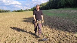 Ein Mann läuft mit einem Metalldetektor über einen Acker.