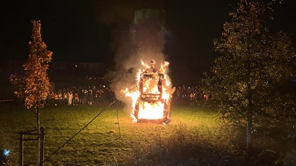 Eine brennende Strohmühle im Vordergrund, staunende Kinder und Erwachsene im Hintergrund.