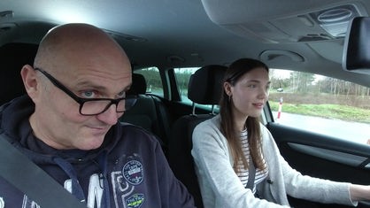 Ein Mann und eine junge Frau sitzen im Auto, die junge Frau am Steuer.
