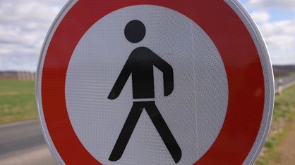 Man sieht ein "Fußgänger verboten" Schild, auf dem ein schwarzes Männchen in einem roten Kreis abgebildet ist. 