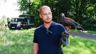 Ein Mann mit Brille und dunkelblauem T-Shirt mit einem Greifvogel auf dem Arm